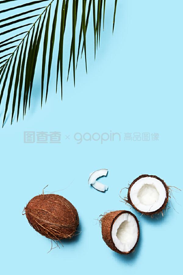 一片椰子和整個椰子,在藍色背景上有一片棕櫚綠葉。食物成分。平鋪。一個由有機的一半和一個椰子組成的美麗組成的藍色背景裝飾著一塊飾板,上面有一片平鋪。